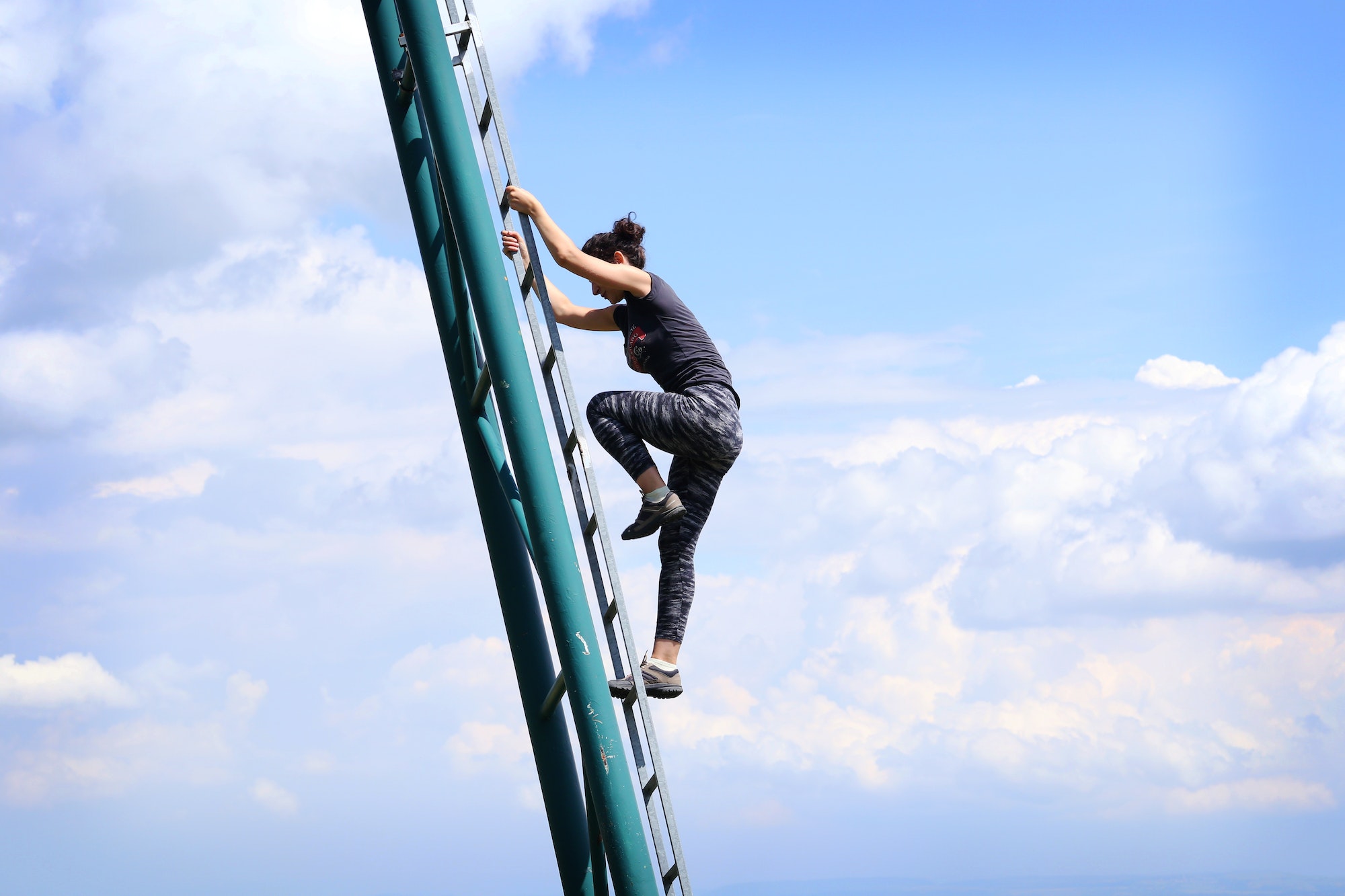 Woman climbing metal ladder on blue sky background. Ambition and determination.